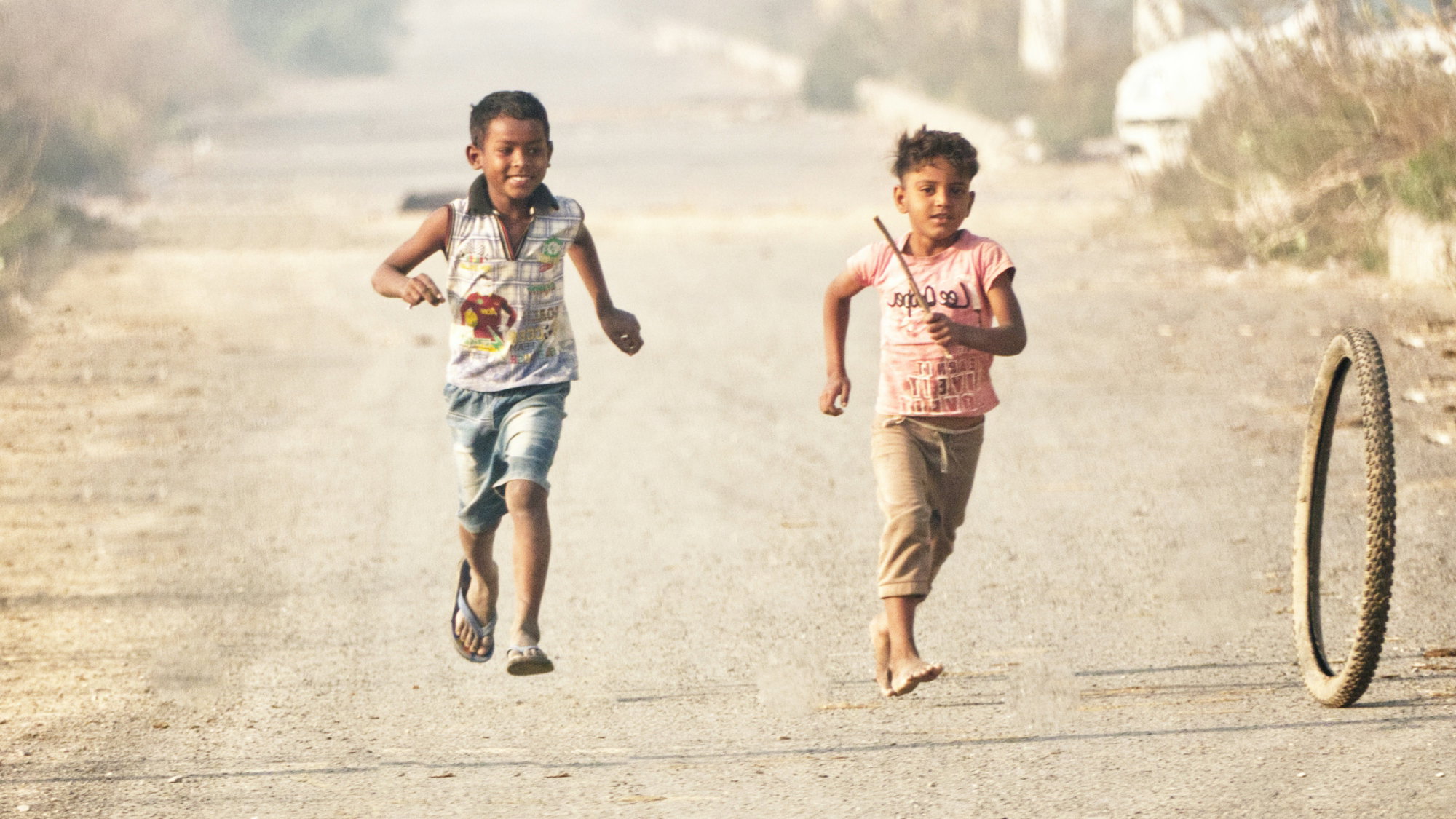 a couple of kids running down a dirt road